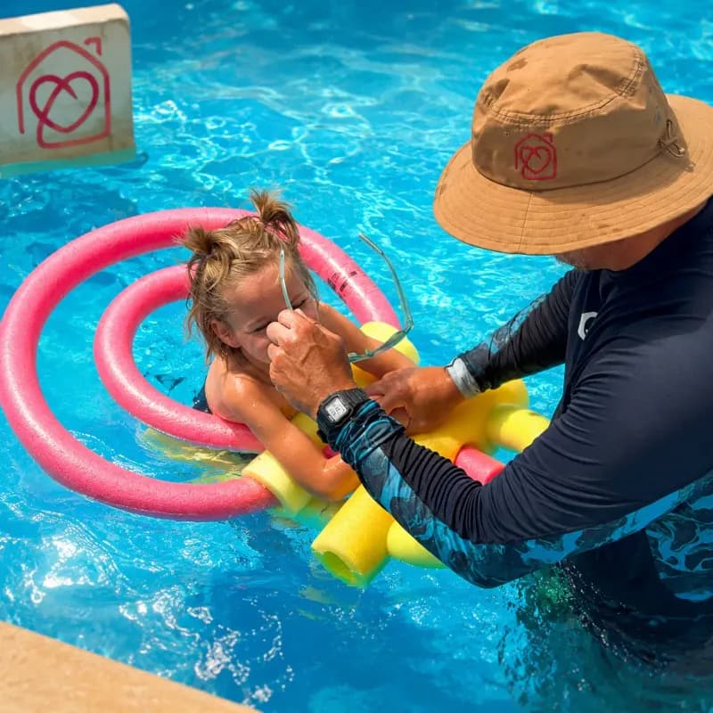 Instructor ayudando a una niña durante una clase de natación infantil en la piscina de Casa Ángeles en Marbella, con material de flotación y apoyo individual.