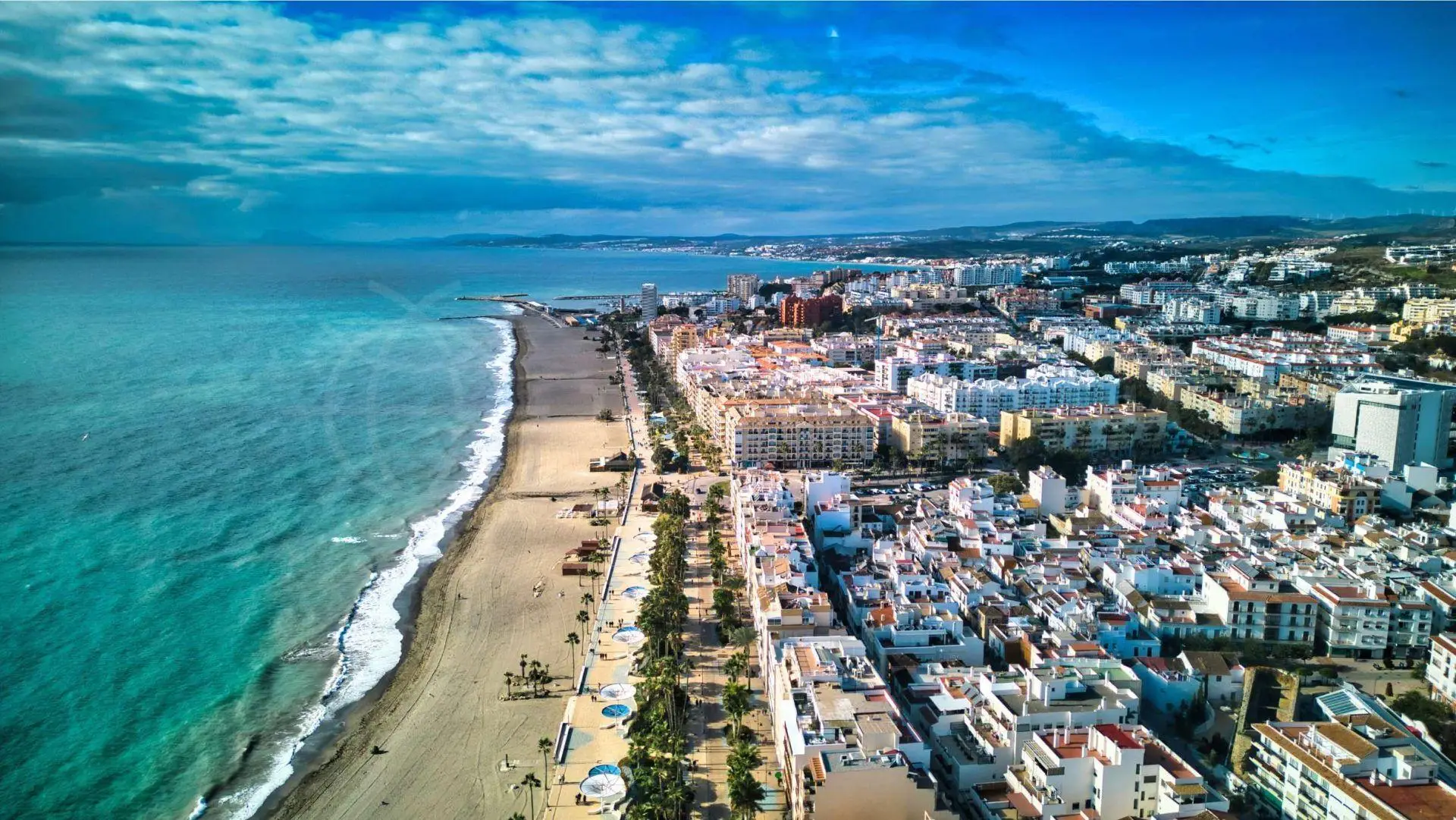 Vista aérea de Estepona de playa, paseo bordeado de palmeras y edificios costeros coloridos en Costa del Sol