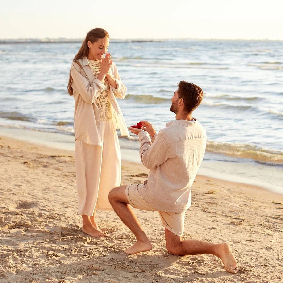 Pareja en una playa junto al mar, con un hombre arrodillado mostrando un anillo a su pareja, imagen asociada a la experiencia ¿Y mi anillo pa’ cuándo?