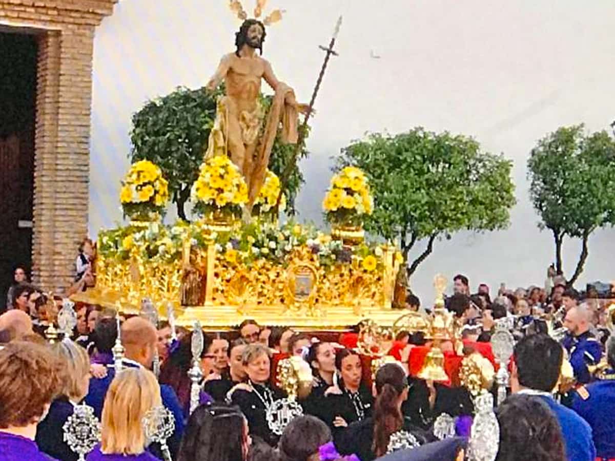 Procesión del Resucitado en Marbella durante el Domingo de Resurrección, con el trono dorado de Cristo Resucitado rodeado de público, músicos y cortejo en la Plaza de la Iglesia.