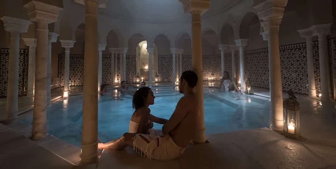 Pareja disfrutando de una experiencia romántica en los baños árabes de Hammam Al Ándalus Málaga, con piscina interior iluminada y ambiente relajante para San Valentín.