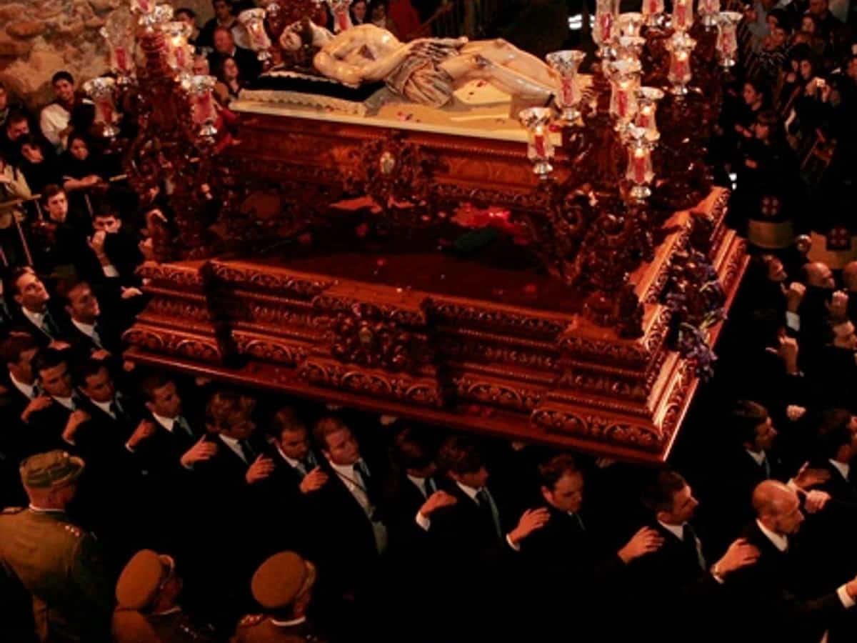 Procesión del Santo Sepulcro en Marbella durante el Viernes Santo, con el Cristo Yacente sobre un trono oscuro rodeado de portadores, legionarios y público en una escena nocturna de gran solemnidad.