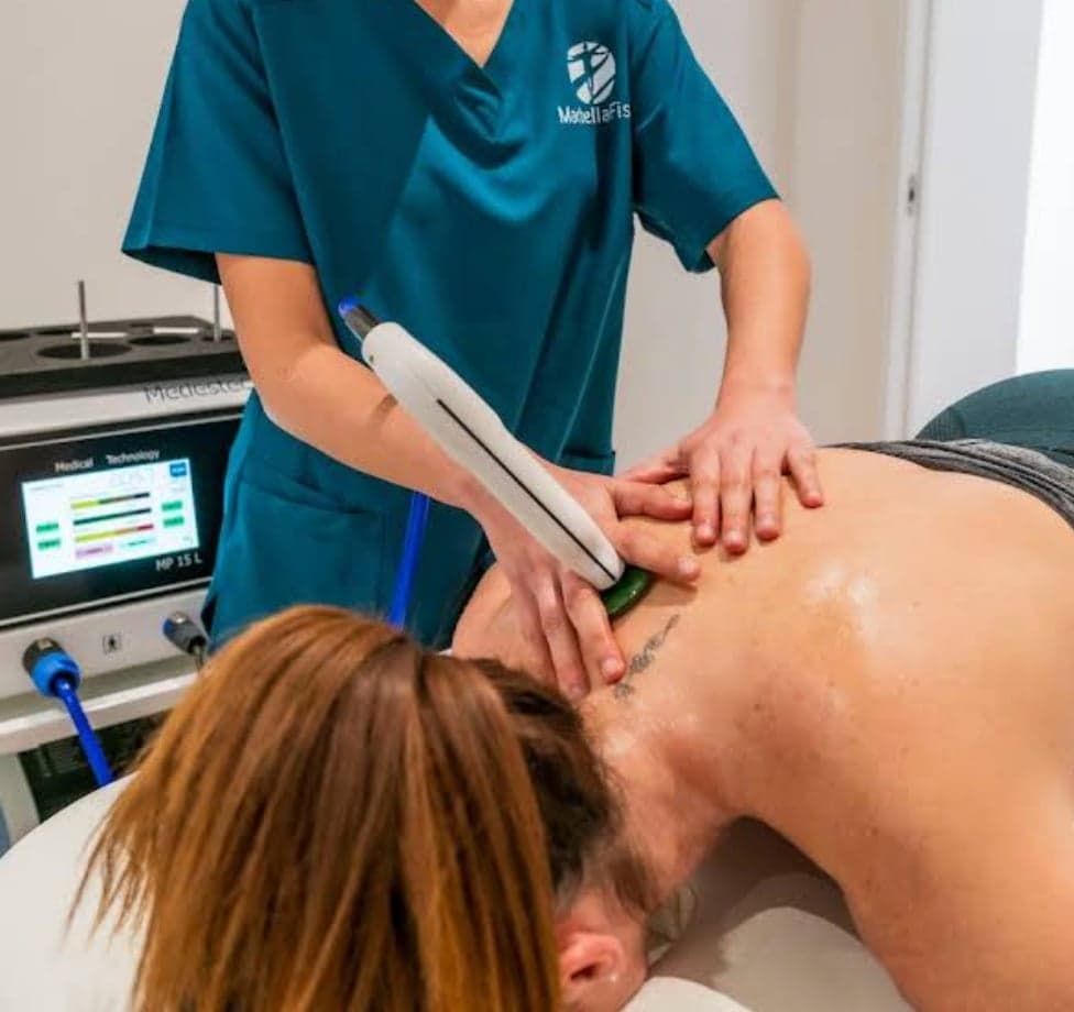 Fisioterapeuta aplicando tratamiento de diatermia/ondas en espalda de paciente con dispositivo profesional en clínica.